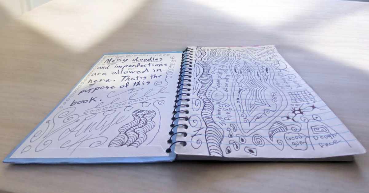 A spiral-bound notebook is open on a light-colored surface, with two pages filled with handwritten text and doodles. The left page reads, "Messy doodles and imperfections are allowed in here. That’s the purpose of this book." Surrounding the text are swirly patterns and abstract designs, including curved lines and shapes. The right page is filled with various intricate doodles, including wavy patterns, spirals, and abstract shapes, along with small handwritten notes. The notebook and its creative contents appear to be illuminated by soft natural light.