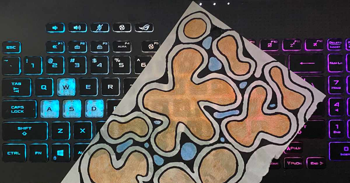 A piece of abstract artwork with organic, amoeba-like shapes in shades of peach, blue, and black lies on top of a backlit keyboard. The keyboard glows with blue lighting on the left and pink on the right.