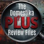Graphic of a large magnifying glass centered over a dark, grungy background with circuit-board patterns. Inside the lens, bold text reads “The Domestika PLUS Review Files,” with “PLUS” in large red letters and the rest in white. The magnifying glass handle extends toward the lower right.